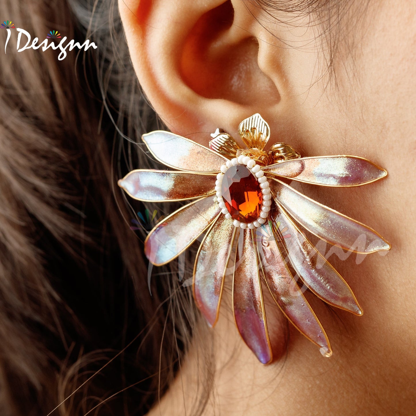 Close-up of a decorative earring worn on an ear, with 'iDesignn' branding.