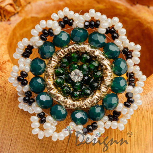 Decorative brooch with green and black stones on a wooden surface