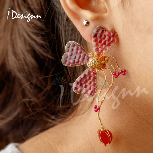 Close-up of a butterfly-shaped earring with pink and gold details worn by a person.