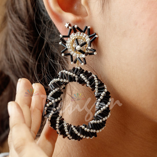 Close-up of a person wearing black and white beaded hoop earrings.