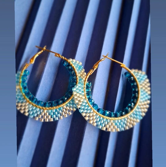 Gold hoop earrings with blue and white beads on a striped background