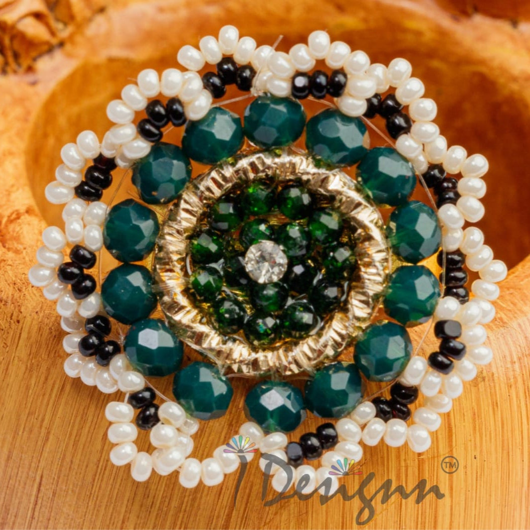 Decorative brooch with green and black stones on a wooden surface